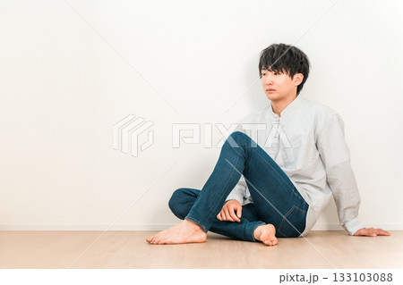 白い壁のリビングに座るジーンズ姿の若いアジア人男性 133103088