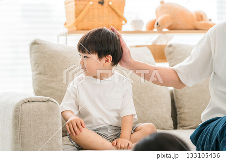 リビングのソファーに座る男の子と頭を撫でる父親 133105436