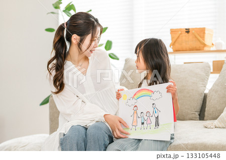 リビングのソファーでお絵描きした絵を見せる女の子と母親 リビングのソファーでお絵描きした絵を見せる女の子と母親 133105448