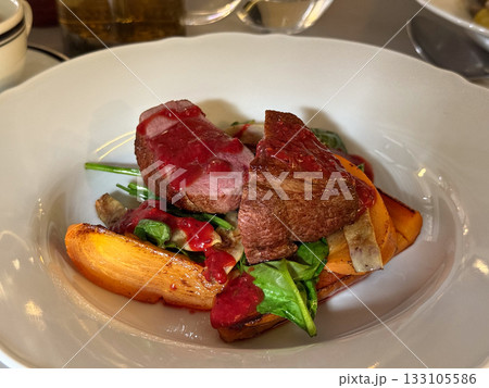 Roasted meat with red sauce and vegetables close-up. Gourmet presentation, contrast, and refined dining atmosphere expressing creativity and taste. 133105586