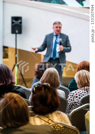 Professional business presentation in a conference hall with audience listening attentively Professional business presentation in a conference hall with audience listening attentively 133107494