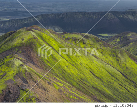 Vibrant green moss covered hills with dark volcanic rock, a dramatic ridge, and a flat plain in Iceland's unique volcanic terrain. Vibrant green moss covered hills with dark volcanic rock, a dramatic ridge, and a flat plain in Iceland's unique volcanic terrain. 133108048