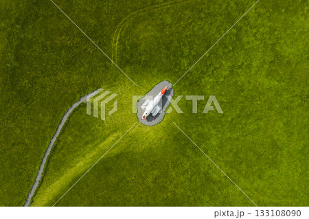 An aerial view shows a white Abandoned U.S. Navy Douglas C 117D aircraft monument with a red nose on a circular gravel area, surrounded by a vast green field and a narrow path in Iceland 133108090