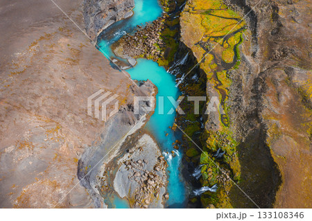 Turquoise river flows through a rugged canyon in Iceland, surrounded by earthy brown terrain, green moss, and cascading waterfalls. Turquoise river flows through a rugged canyon in Iceland, surrounded by earthy brown terrain, green moss, and cascading waterfalls. 133108346