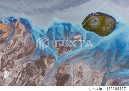 Vibrant blue glacial streams flow through brown terrain, surrounding a moss covered island in Iceland. The intricate patterns create striking contrasts. Vibrant blue glacial streams flow through brown terrain, surrounding a moss covered island in Iceland. The intricate patterns create striking contrasts. 133108357
