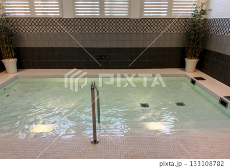 Modern spa interior featuring a tranquil thermal pool with rippling water and a stainless steel handrail Modern spa interior featuring a tranquil thermal pool with rippling water and a stainless steel handrail 133108782