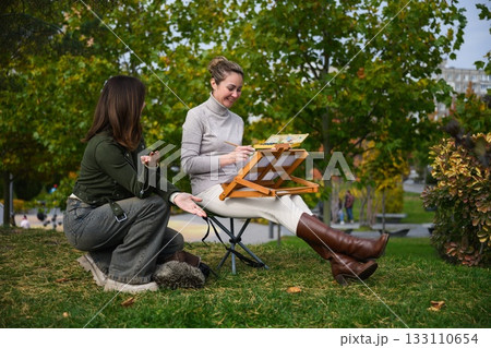 Two women talking while painting outdoors in park. Two women talking while painting outdoors in park. 133110654