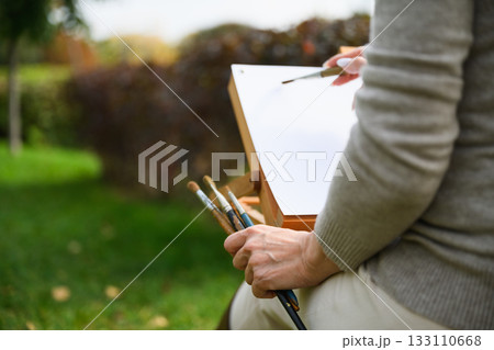 Close-up of artist painting on blank canvas outdoors. Close-up of artist painting on blank canvas outdoors. 133110668