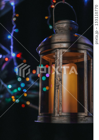 Rustic metal lantern with candle and colorful Christmas lights in dark evening background Rustic metal lantern with candle and colorful Christmas lights in dark evening background 133110770