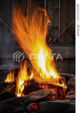 Campfire burning with bright orange flames and glowing wood, detailed view of fire texture and warm natural light in rustic setting Campfire burning with bright orange flames and glowing wood, detailed view of fire texture and warm natural light in rustic setting 133110784