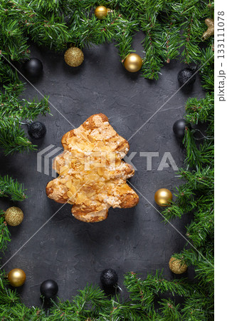 Festive christmas tree pastry with almonds surrounded by pine and baubles on dark stone background Festive christmas tree pastry with almonds surrounded by pine and baubles on dark stone background 133111078