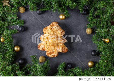 Festive christmas tree pastry with almonds surrounded by pine and baubles on dark stone background Festive christmas tree pastry with almonds surrounded by pine and baubles on dark stone background 133111080