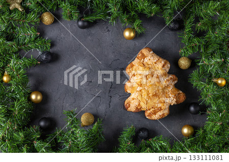 Festive christmas tree pastry with almonds surrounded by pine and baubles on dark stone background Festive christmas tree pastry with almonds surrounded by pine and baubles on dark stone background 133111081