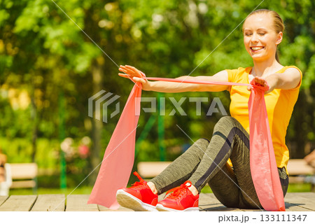 Girl doing exercise outdoor, using resistance fit band. 133111347