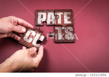 Hands assembling puzzle pieces forming the words Rate Cuts, concept of finance economy and interest 133111950
