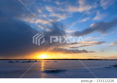 A tranquil winter scene shows a glowing sunset over a snow covered landscape 133112226