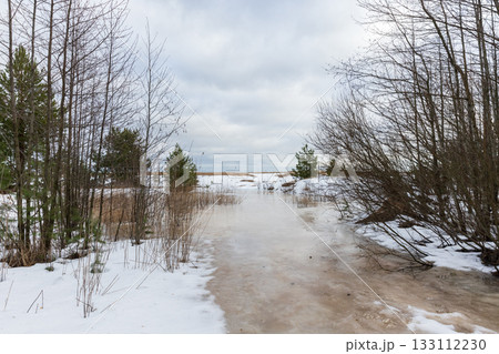 A quiet winter landscape shows an icy path winding through a snow-dusted forest A quiet winter landscape shows an icy path winding through a snow-dusted forest 133112230