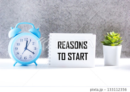 The phrase REASONS TO START in a notebook with an alarm clock and a flower on the table The phrase REASONS TO START in a notebook with an alarm clock and a flower on the table 133112356