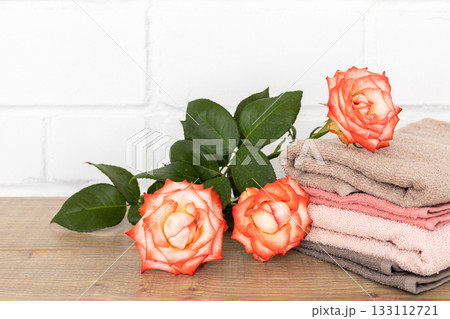 Stack of soft terry towels with rose flowers on the wooden boards Stack of soft terry towels with rose flowers on the wooden boards 133112721