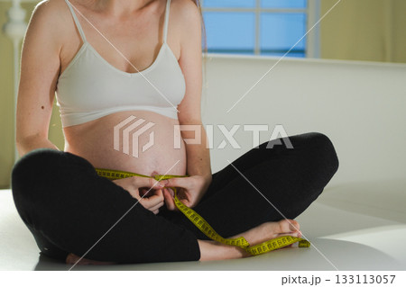 Pregnancy motherhood. Pregnant woman measuring big belly. Girl measuring her belly with tape to keep track of her fetus development. Woman enjoying pregnancy. Maternity tenderness parenthood new life 133113057