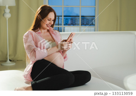 Pregnancy motherhood. Pregnant woman with smartphone typing scrolling at home. Woman with cell phone enjoying pregnancy surfing internet using social media apps. Mobile application for pregnant women 133113059