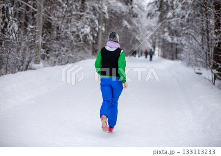 Rear view warmly dressed woman running winter park Rear view warmly dressed woman running winter park 133113233