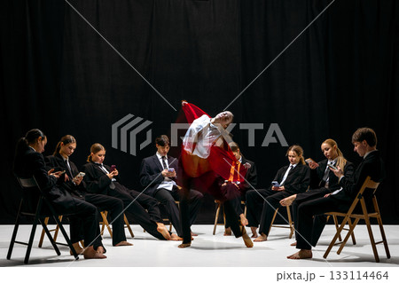 Expressive leap of performer in red jacket with motion-blur amid colleagues absorbed in smartphones 133114464