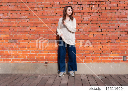 赤レンガの壁の前に立つ女性 133116094