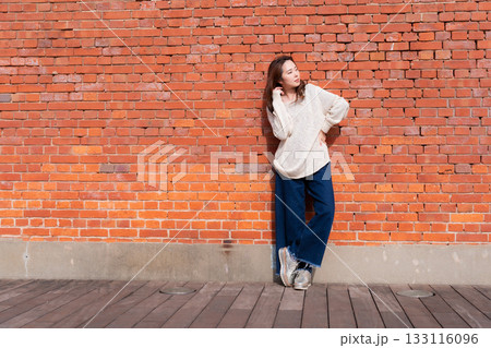 赤レンガの壁の前に立つ女性 133116096