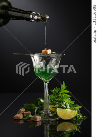 Absinthe is poured from an vintage bottle into a glass. Absinthe is poured from an vintage bottle into a glass. 133116908