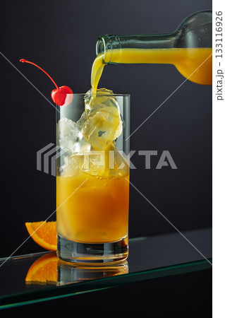 Orange juice is poured into a glass with ice. Orange juice is poured into a glass with ice. 133116926