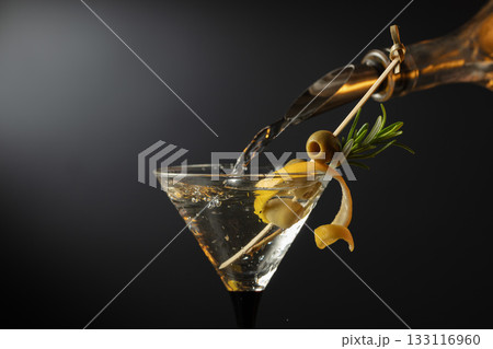 Classic dry martini cocktail with green olives, lemon peel, and rosemary on a black background. Classic dry martini cocktail with green olives, lemon peel, and rosemary on a black background. 133116960