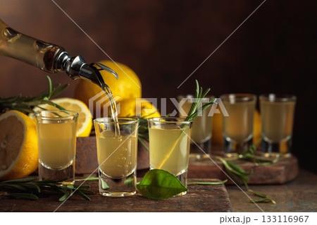 Italian liqueur Limoncello with fresh lemons and rosemary branches. 133116967