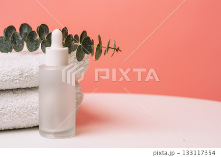 Serum bottle on soft towels with eucalyptus branch, pastel background 133117354