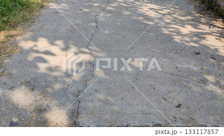 Shadow cast across cracked cement road showing urban wear and surface decay 133117857