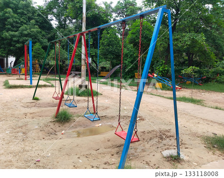 swings on metal frame in outdoor playground, surrounded by green trees, slides, and seesaws, fun recreation for children swings on metal frame in outdoor playground, surrounded by green trees, slides, and seesaws, fun recreation for children 133118008