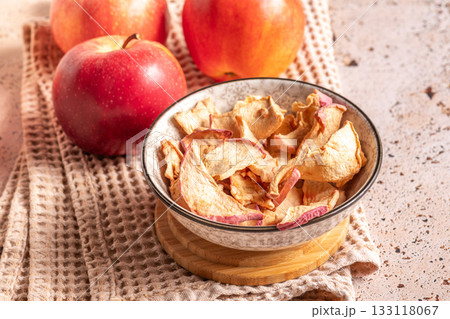 Dried apple slices in a bowl with fresh apples on sunny kitchen 133118067