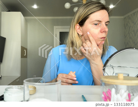 In the soft morning light, a young lady applies her daily makeup while looking into the mirror to ensure precise application. 133118075