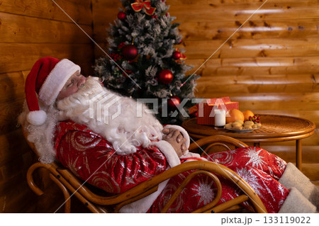 Santa Claus peacefully asleep in a chair, with a festive Christmas tree Santa Claus peacefully asleep in a chair, with a festive Christmas tree 133119022