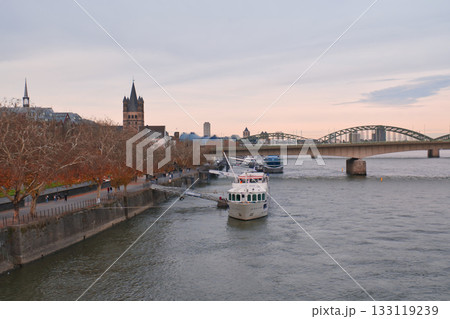 Cruise boat docked by riverside in city during evening light with historic buildings nearby 133119239