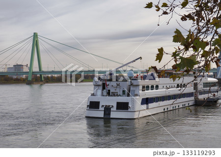 Cruise ship docked by the river with a green bridge in the background during cloudy weather Cruise ship docked by the river with a green bridge in the background during cloudy weather 133119293