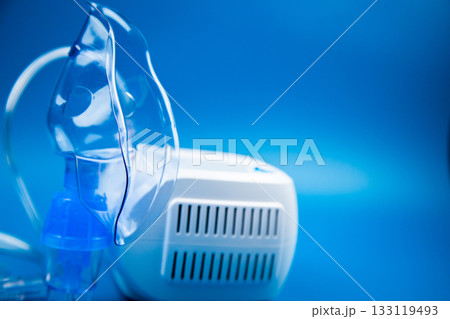 Close-up side view of a blue mask and a camera on a blue background with space for text. The concept of treating respiratory diseases, lung diseases, prevention and self-care. High quality photo Close-up side view of a blue mask and a camera on a blue background with space for text. The concept of treating respiratory diseases, lung diseases, prevention and self-care. High quality photo 133119493