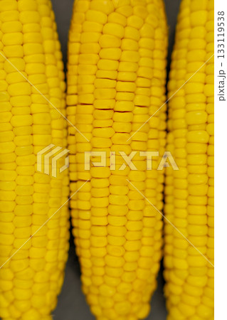 Vertical close-up photo of yellow peeled corn cobs with a clear texture of large grains lying in a row on a dark background. The concept of healthy nutrition, natural iron, corn cultivation. High 133119538
