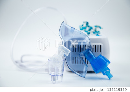 Close-up of an inhalation bowl with an ampoule of medicinal solution in it against the background of a blue breathing mask and a device on a white background. The concept of treatment of respiratory 133119539