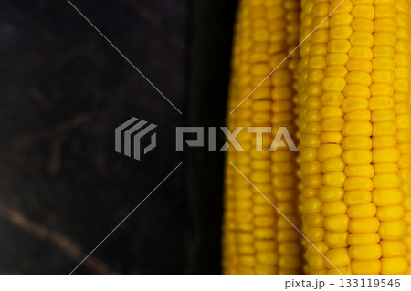 Close-up of yellow ripe peeled ears of corn with large grains lying on the side on a dark background with space for text. The concept of healthy nutrition, natural iron, corn cultivation. High quality 133119546