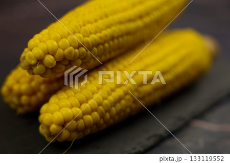 Three yellow peeled ears of corn with large grains lie on a black stone plank against a dark background in the center. The concept of healthy nutrition, natural iron, corn cultivation. High quality Three yellow peeled ears of corn with large grains lie on a black stone plank against a dark background in the center. The concept of healthy nutrition, natural iron, corn cultivation. High quality 133119552