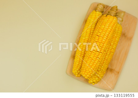 Top view of yellow ripe peeled ears of corn with large grains lying on a wooden board on the side on a yellow background with space for text. The concept of healthy nutrition, natural iron, corn Top view of yellow ripe peeled ears of corn with large grains lying on a wooden board on the side on a yellow background with space for text. The concept of healthy nutrition, natural iron, corn 133119555