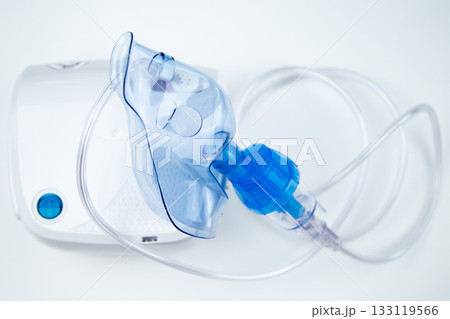 Close-up of a blue inhalation mask lying on a white machine on a white background. The concept of inhalation of vapors, treatment of the respiratory tract, inhalation, prevention of pulmonary diseases 133119566