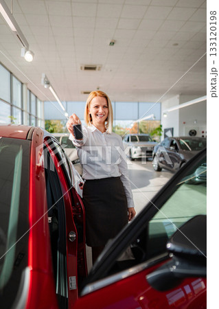 Happy young adult woman holding car keys at dealership Happy young adult woman holding car keys at dealership 133120198