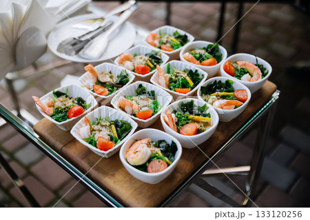Mini shrimp seaweed salads in white bowls on a catering tray at an outdoor event Mini shrimp seaweed salads in white bowls on a catering tray at an outdoor event 133120256